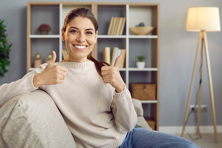 Smiling person giving thumbs up while sitting on a sofa in a tidy living room, representing satisfaction with cleaning services.