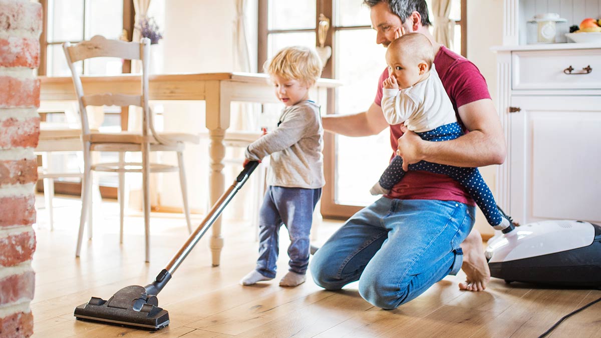 Father and children vacuuming hardwood floors together in a bright home, showing consistent cleaning habits and recurring house cleaning in Eastside family homes.