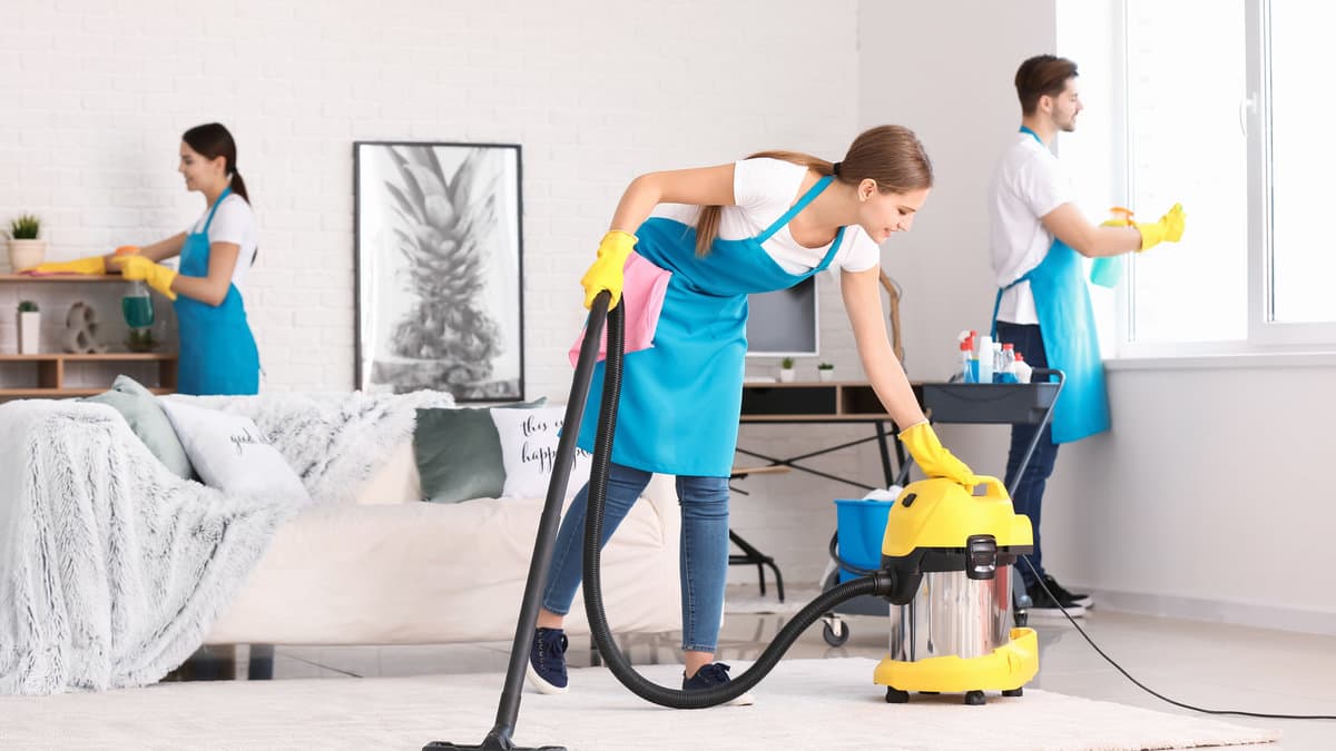 Cleaning team vacuuming, wiping, and polishing a modern living room.
