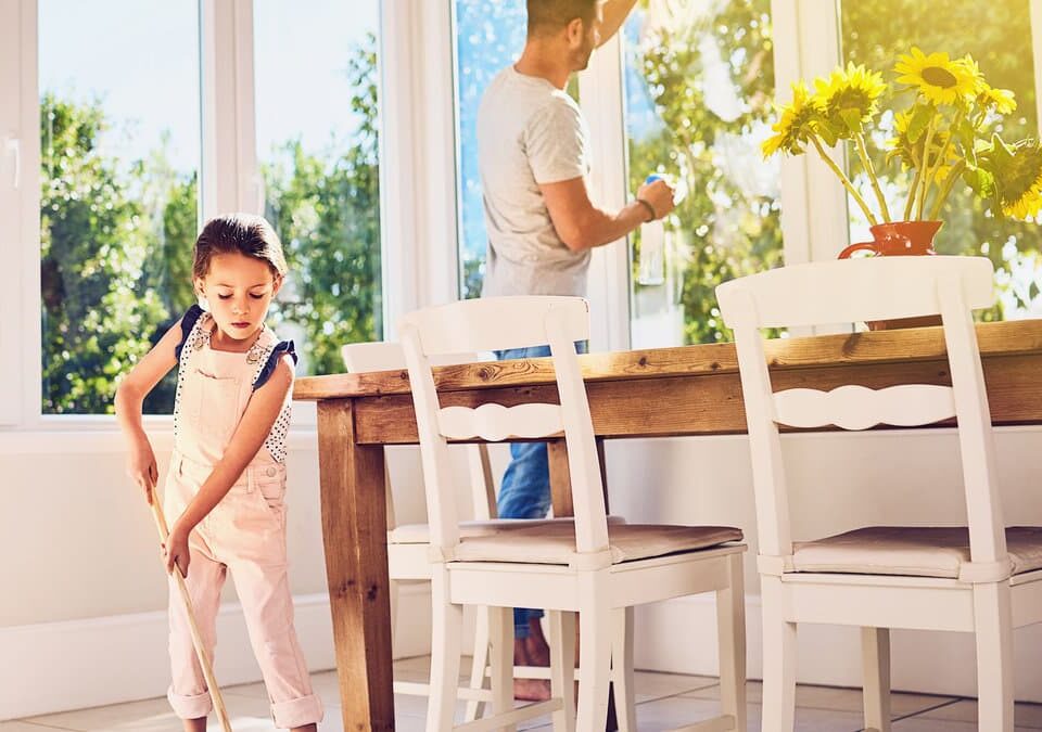 Spring house cleaning in an Issaquah home with a parent cleaning windows and a child sweeping the floor
